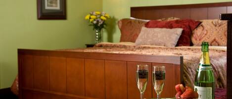Una cama bien hecha con cabecera de madera, una mesita de noche con una bandeja que contiene copas de champán, una botella de champán y un cuenco de fresas.