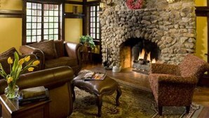 A cozy living room with a stone fireplace, leather furniture, and a large window. - Hilltop Manor Bed and Breakfast (Hot Springs)