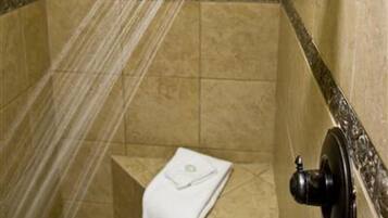 A shower with a towel hanging on the wall, a tiled floor, and a showerhead.