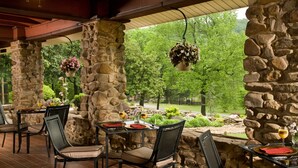A covered patio with stone pillars, outdoor seating, and hanging flower baskets. - Hilltop Manor Bed and Breakfast (Hot Springs)