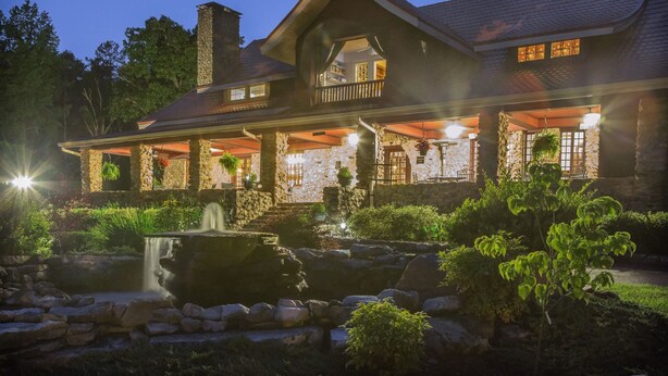 A large, stone-clad house with a prominent balcony, a stone fountain, and a well-maintained garden. - Hilltop Manor Bed and Breakfast (Hot Springs)