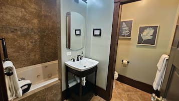 Un baño con bañera, lavamanos, espejo y retrete. Hay toallas colgadas en la pared y una decoración con una hoja enmarcada.