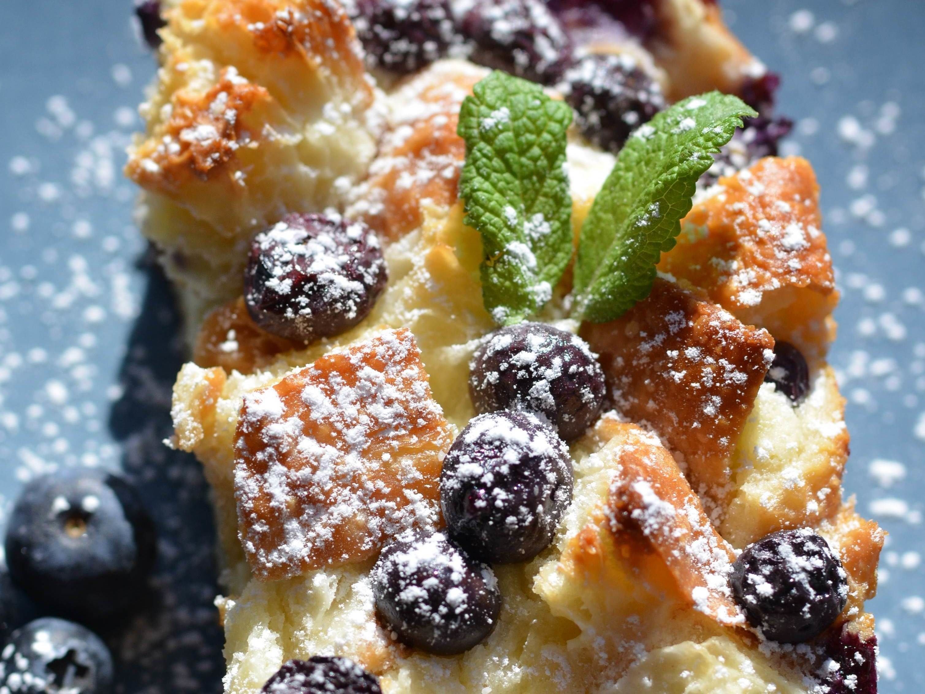 En bit blåbärscrème brûlée, garnerad med florsocker och myntablad.