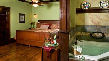 A well-appointed bedroom with a large bed, a wooden headboard, a bedside table with a tray holding glasses and a bottle, and a marble-tiled bathroom with a bathtub.