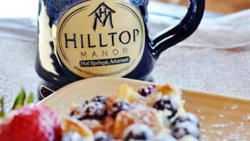 A mug with the text "HILLTOP MANOR Hot Springs, Arkansas" and a plate of food with berries and whipped cream.