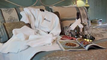 A neatly made hotel bed with a white robe, a bottle, glasses, and a menu on the bed.