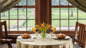 A dining table set for two with a vase of tulips, two glasses of orange juice, and plates of food. - Hilltop Manor Bed and Breakfast (Hot Springs)
