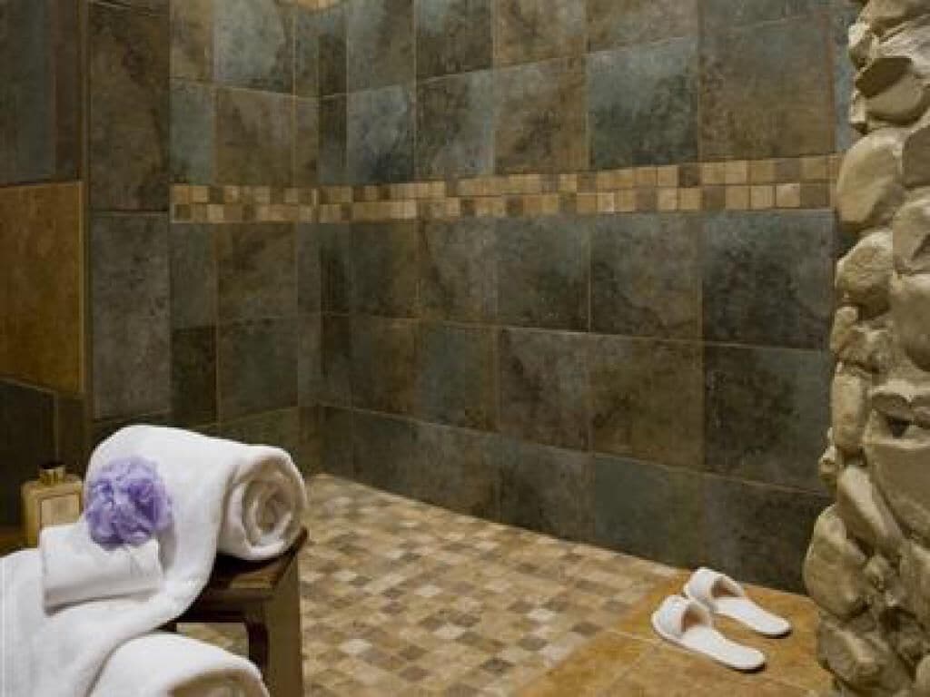 A bathroom with a checkered floor, a stone wall, and a towel and slippers on a bench.