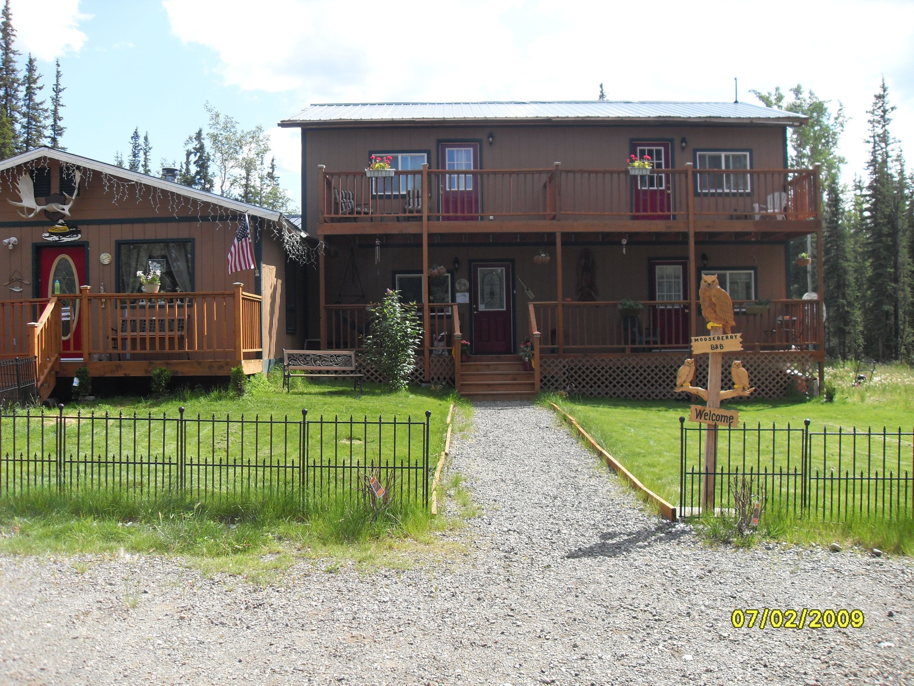 A two-story wooden cabin with a front porch, a mailbox, and a welcome sign.