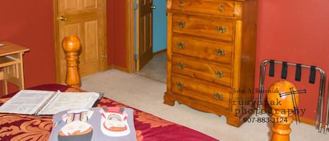 A bedroom with a wooden dresser, a television mounted on the wall, and a bed with a red bedspread.