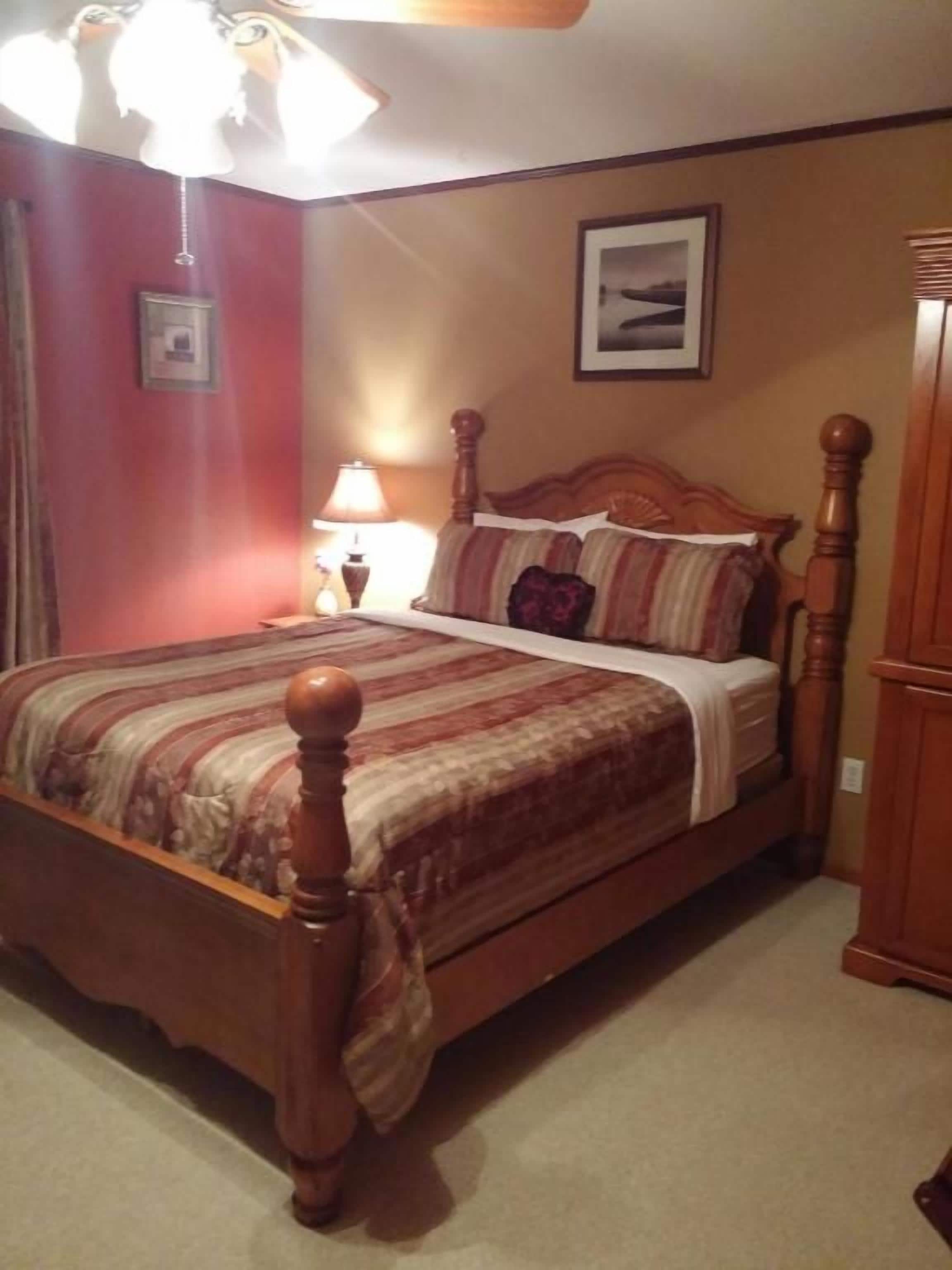 A bedroom with a wooden bed, a nightstand with a lamp, a framed picture on the wall, and a ceiling fan.