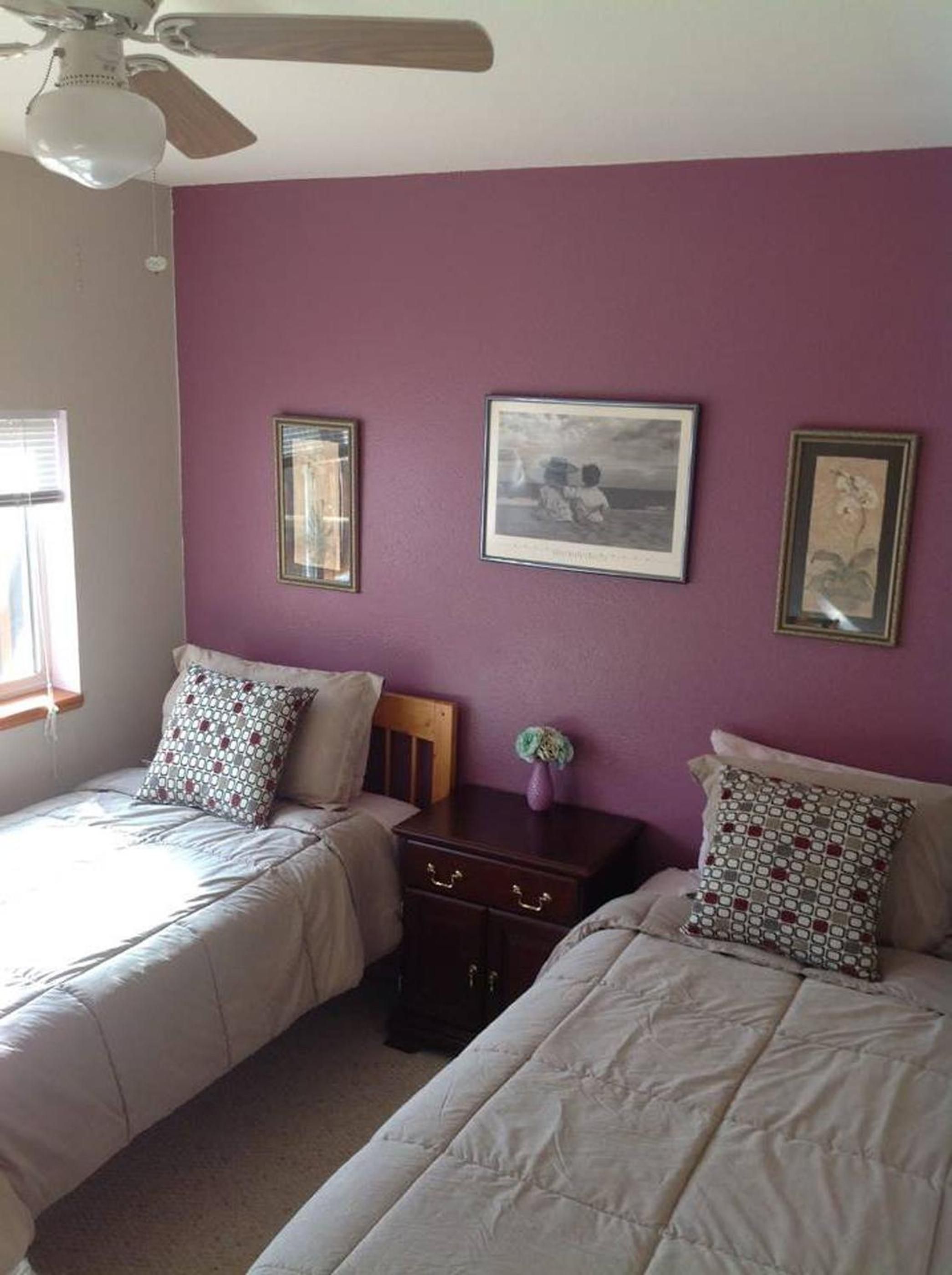 A bedroom with two beds, a ceiling fan, and three framed pictures on the wall.