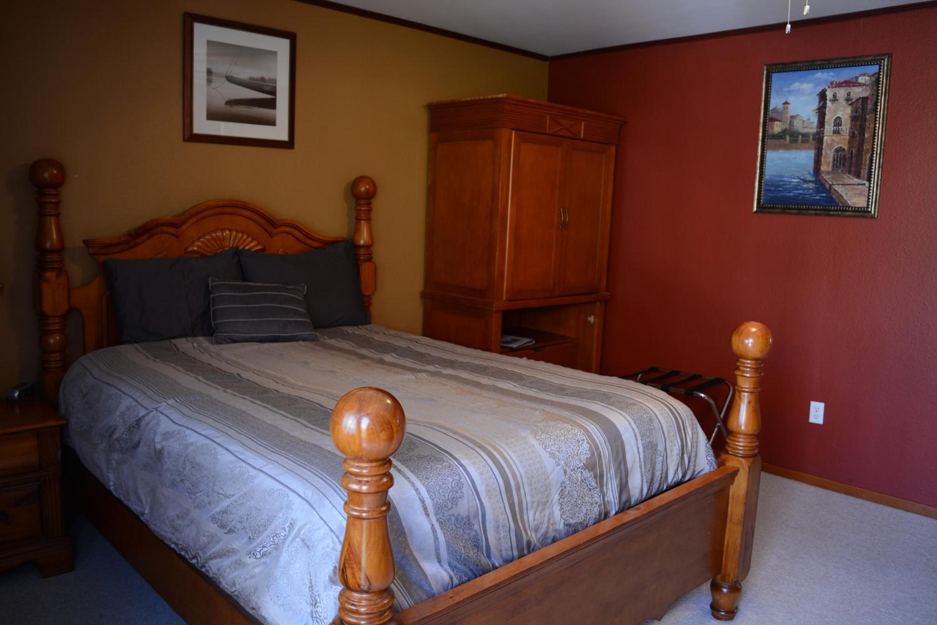 Un dormitorio con una cama de madera, una mesita de noche, un armario y dos cuadros en las paredes.