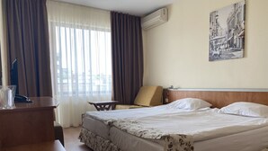 A hotel room with a bed, a desk, a chair, and a window with curtains. - Hotel Atol (Sunny Beach)