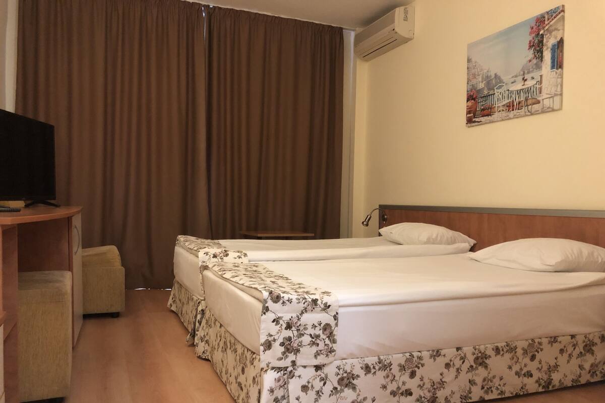 Una habitación de hotel con dos camas, televisión, escritorio y un cuadro en la pared.