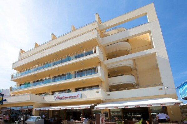 Un hotel de varios pisos con balcones, un restaurante en la planta baja y mesas al aire libre.