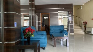 A spacious lobby with a blue sofa, a wooden table, and a potted plant. A staircase with a railing is visible in the background. - Hotel Atol (Sunny Beach)