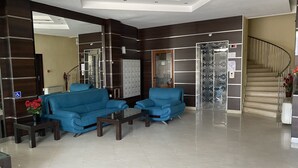 A modern lobby with a blue sofa set, a reception desk, a glass elevator, and a staircase. - Hotel Atol (Sunny Beach)