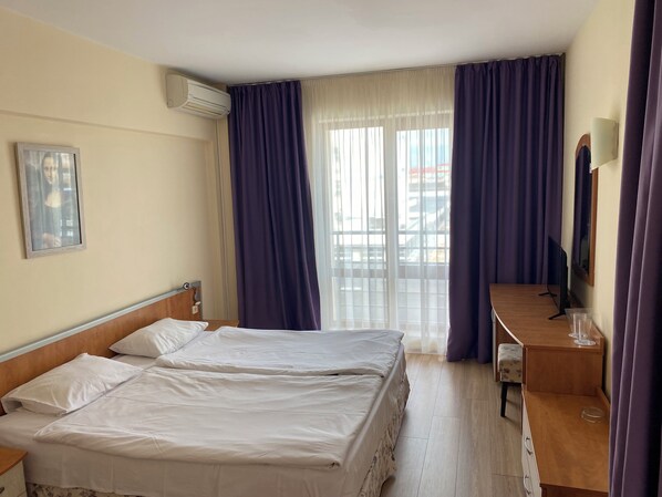 A hotel room with two beds, a desk, a chair, a TV, and a window with curtains. - Hotel Atol (Sunny Beach)