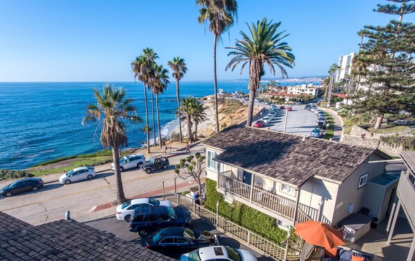 A coastal residential area with parked cars, palm trees, and a view of the sea.