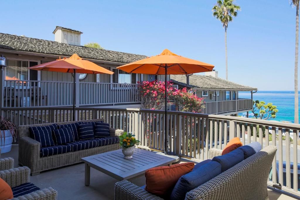 Ein Balkon mit Korbmöbeln, orangefarbenen Sonnenschirmen und Blick auf das Meer.