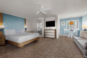 A hotel room with a bed, a desk, a TV, a dining area, and a ceiling fan.