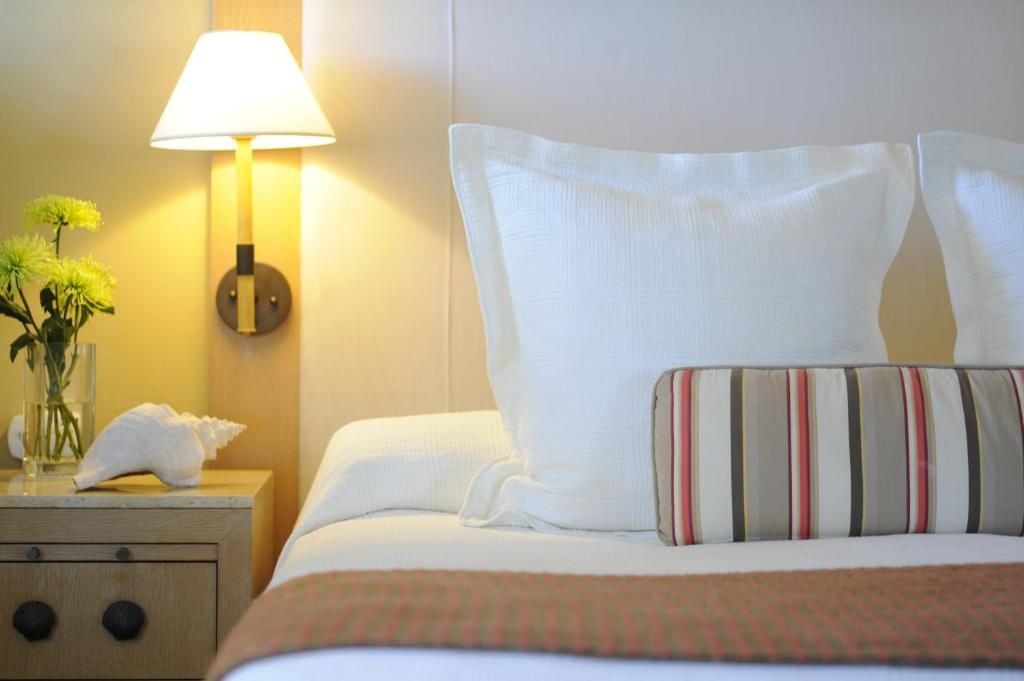 Una habitación de hotel con cama, mesita de noche con lámpara, un florero con flores y una toalla.