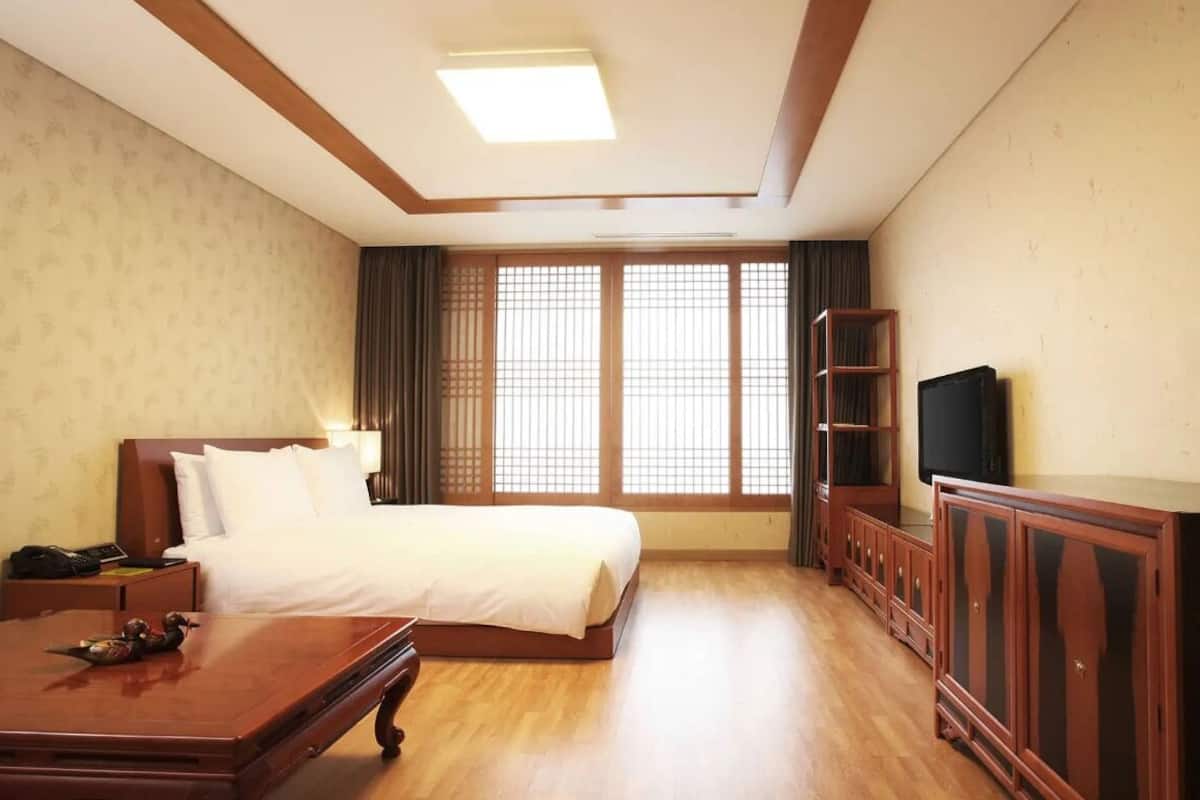 A hotel room with a bed, wooden desk, TV, and traditional decor.