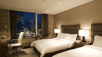 Habitación de hotel con dos camas, un escritorio con lámpara, una silla y vista a la ciudad de noche.