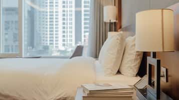 Una habitación de hotel con una cama, una mesita de noche con una lámpara y vistas a edificios altos a través de la ventana.