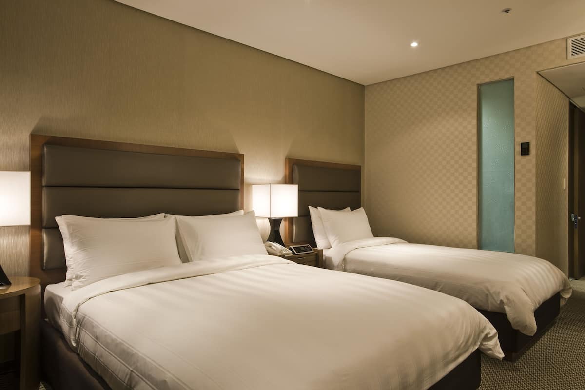 A hotel room with two beds, each with a headboard, bedside tables, and lamps.