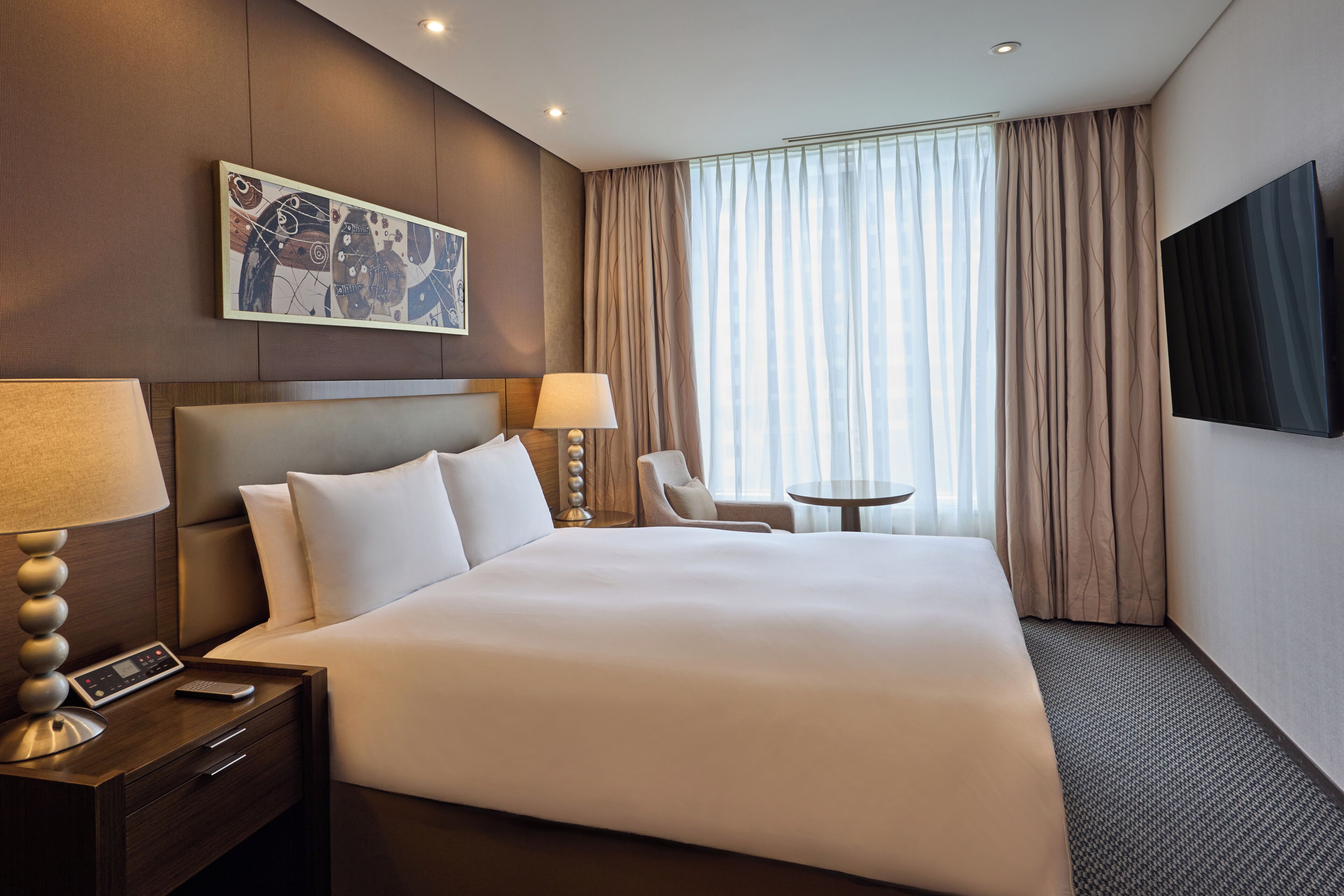 Habitación de hotel con una cama grande, dos mesitas de noche, un escritorio, una silla, un televisor y una ventana con cortinas.
