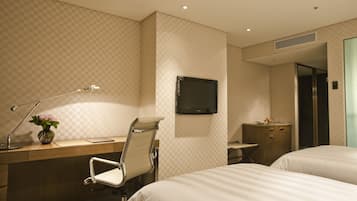 A hotel room with a desk, two beds, a TV, a chair, and a small cabinet.
