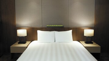 Habitación de hotel con una cama grande, dos mesitas de noche con lámparas y un panel de pared texturizado sobre la cama.