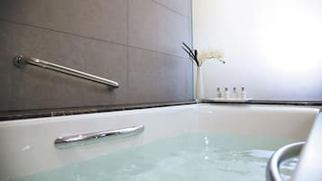 Una bañera con puerta de cristal, un pasamanos y un florero con flores blancas en la pared.