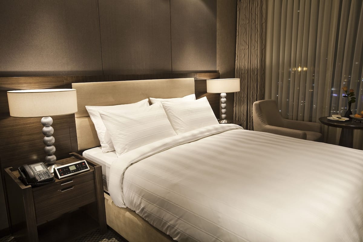 A hotel room with a large bed, two bedside tables with lamps, a chair, and a small table with a vase of flowers.