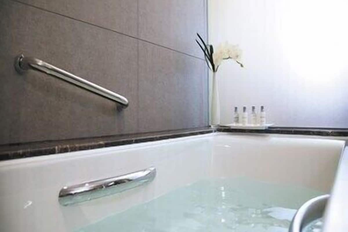 A modern bathroom with a bathtub, a handrail, and a vase with flowers.