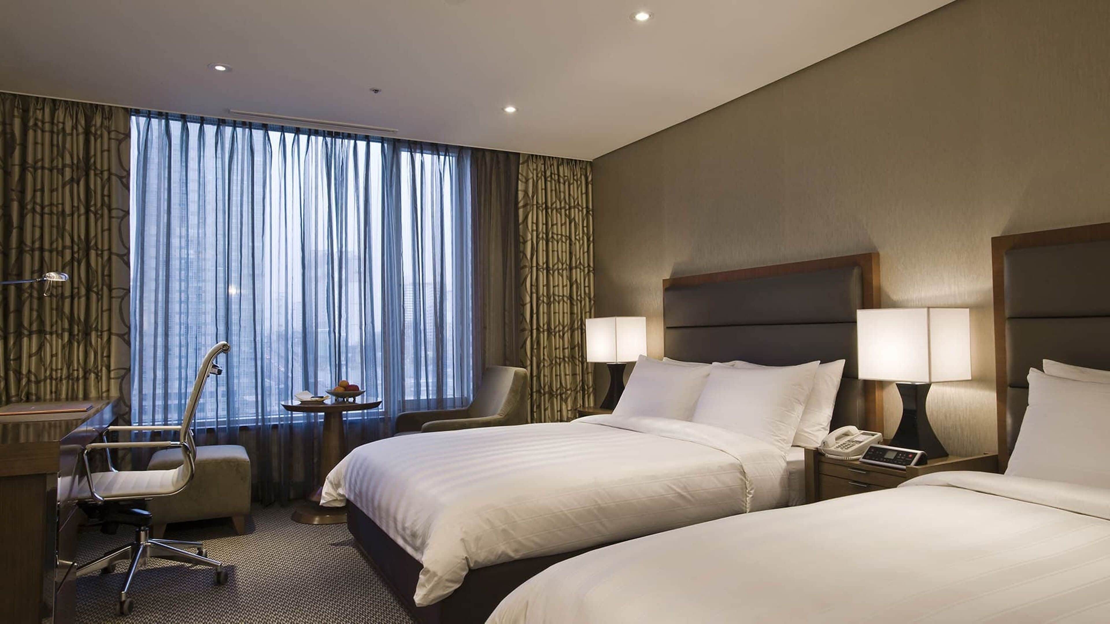 A hotel room with two beds, a desk, a chair, and a window with curtains.