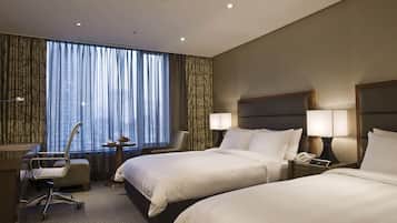A hotel room with two beds, a desk, a chair, and a window with curtains.