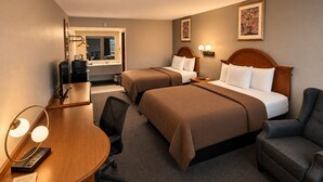Habitación de hotel con dos camas, un escritorio, una silla, un espejo y una mesita de noche con lámpara.