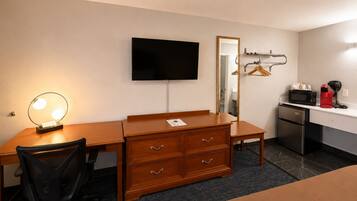 A hotel room with a wooden desk, a chair, a TV, a mirror, a microwave, and a mini-fridge.
