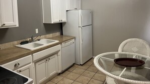 Una cocina compacta con gabinetes blancos, un refrigerador blanco, un lavamanos y una mesa de vidrio con una bandeja.
