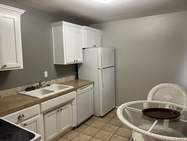 Una cocina compacta con gabinetes blancos, un refrigerador blanco, un lavamanos y una mesa de vidrio con una bandeja.