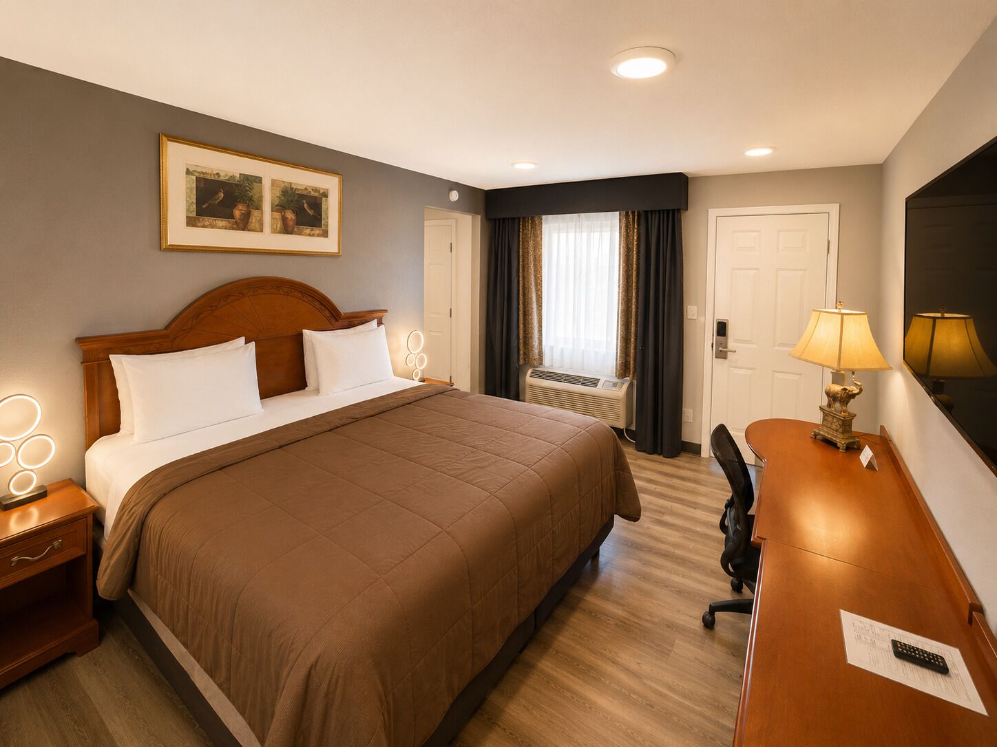 A hotel room with a large bed, bedside lamps, a desk, a chair, and a window with curtains.