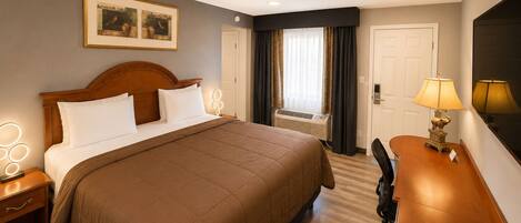 A hotel room with a large bed, bedside lamps, a desk, a chair, and a window with curtains.