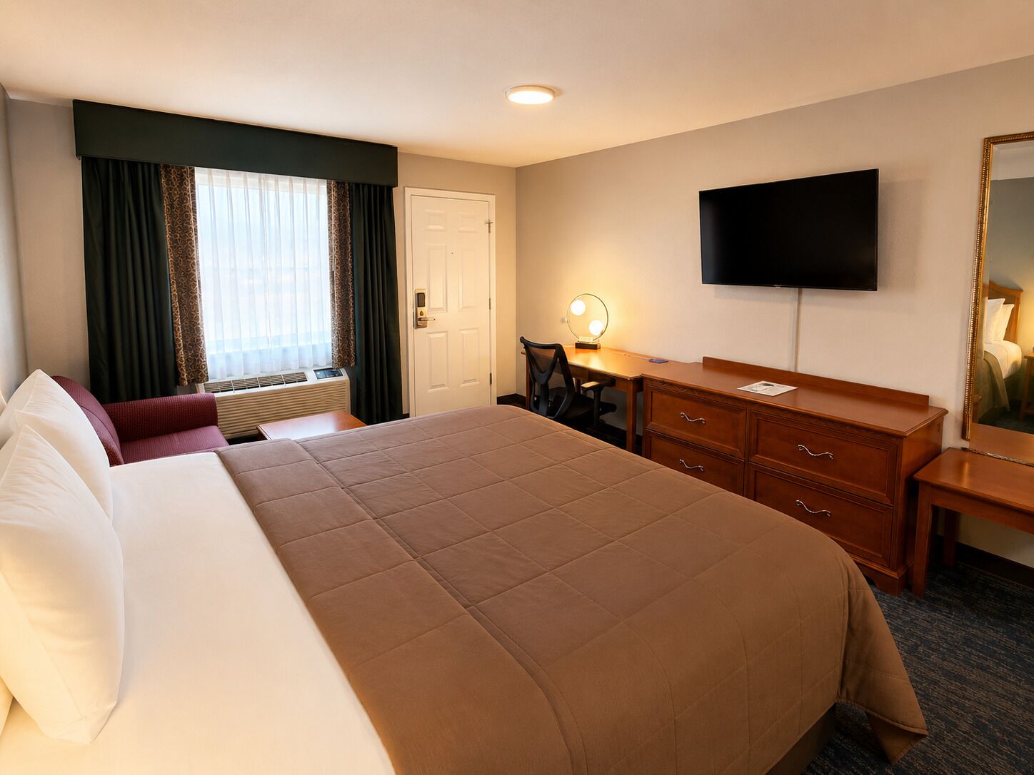 Habitación de hotel con una cama grande, un escritorio con silla, un televisor y un espejo.