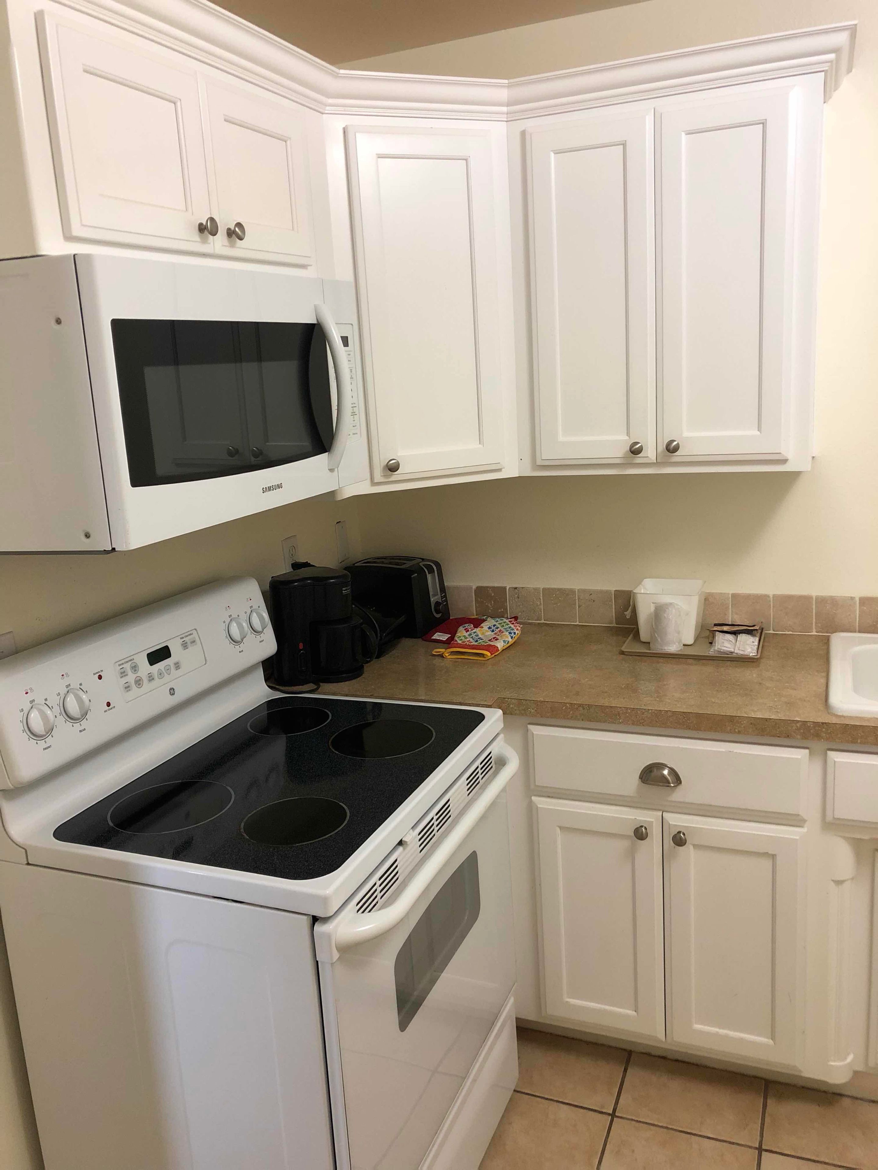A kitchen with white cabinets, a microwave, a stove, and a coffee maker.