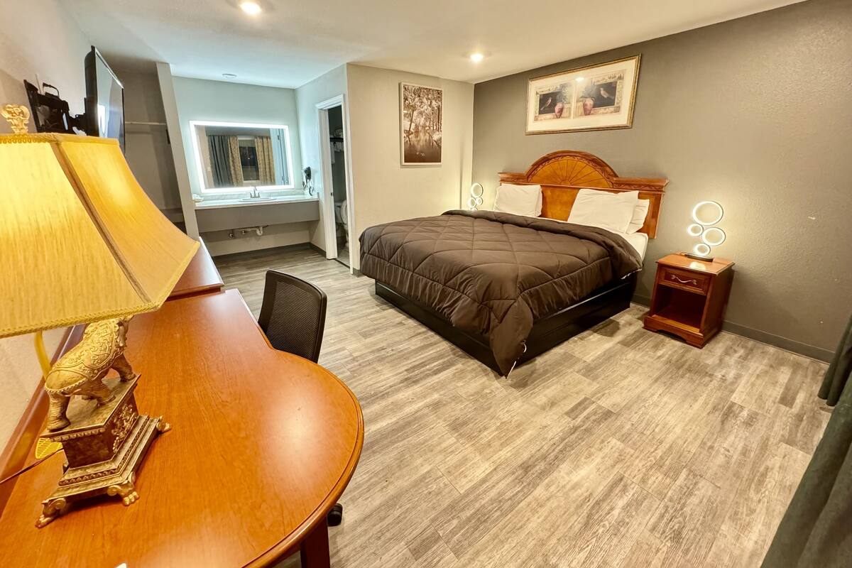 A hotel room with a bed, bedside table, lamp, chair, and a desk with a decorative item.