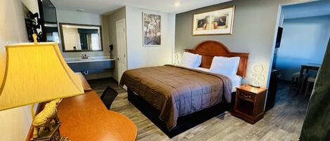 A hotel room with a bed, bedside table, lamp, and a small desk with a decorative item.