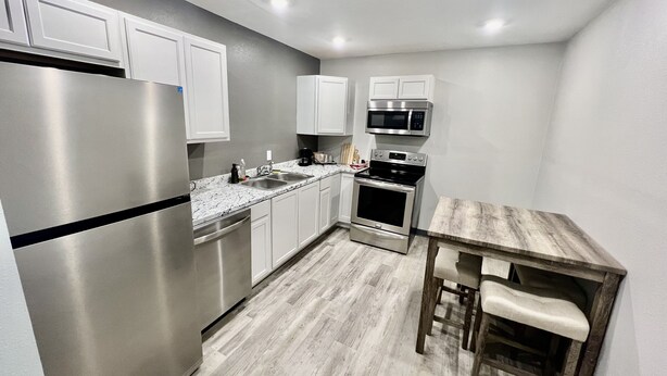 Una cocina compacta con armarios blancos, electrodomésticos de acero inoxidable y una mesa de madera con sillas.
